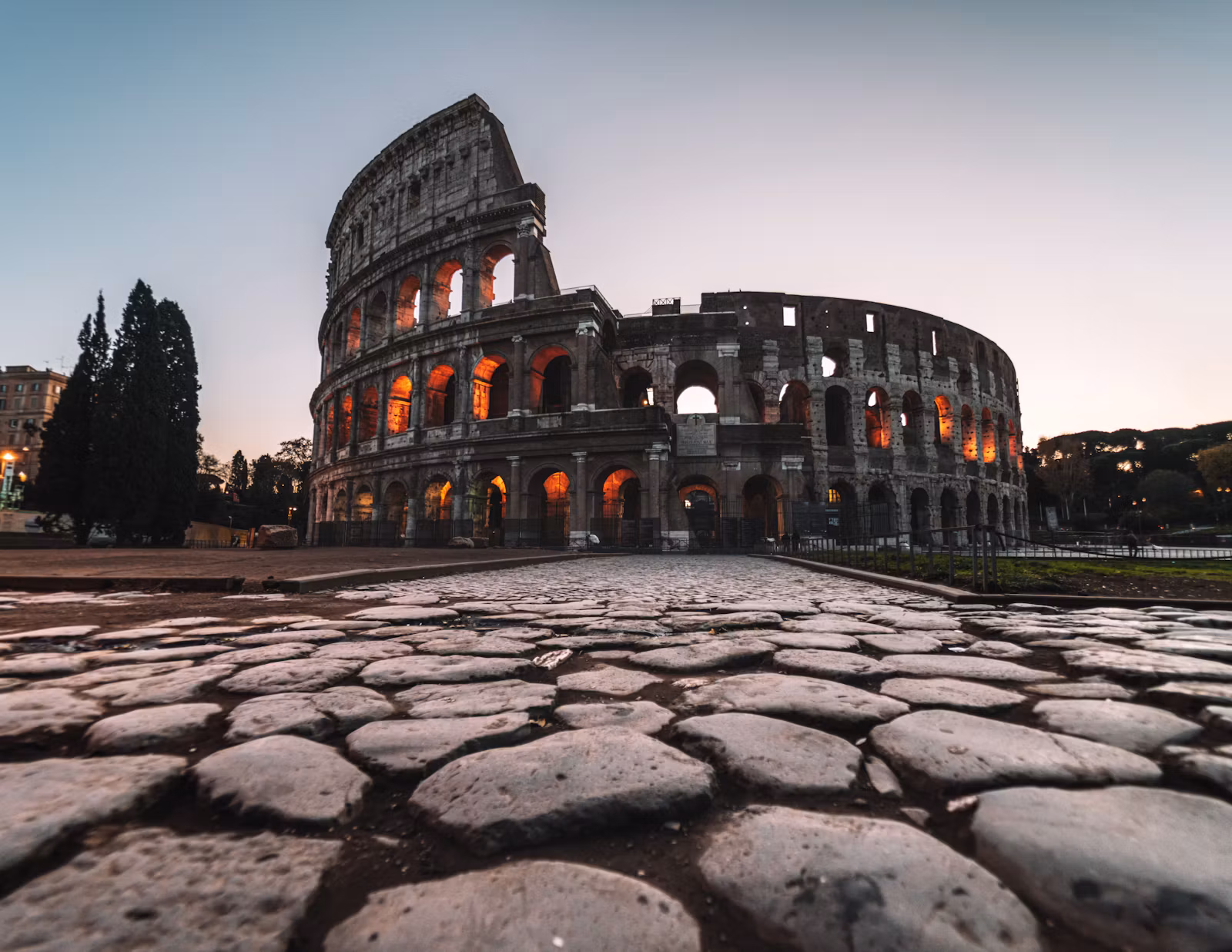 The Colosseum at dawn behind ancient Roman paving stones