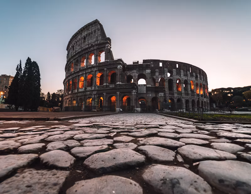 The Colosseum at dawn behind ancient Roman paving stones